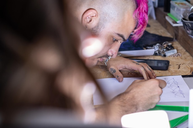 Foto tätowierer entwirft und zeichnet ein tattoo mit einem bleistift auf einem blatt papier, bevor er in seinem tattoo-studio tätowiert