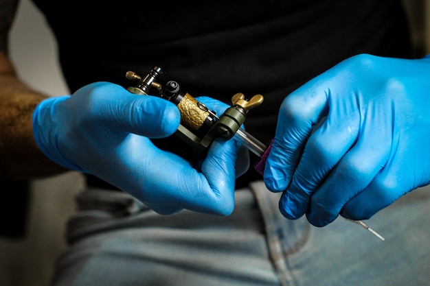 Tätowierer mit blauen Latexhandschuhen, der die Nadel und die Tätowiermaschine vorbereitet.