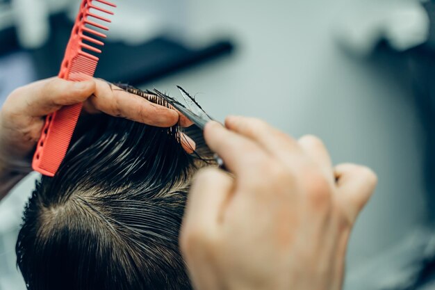 Foto tätowierter friseur schneidet dem kunden die haare mit einer schere aus der nähe. attraktiver mann bekommt einen modus.