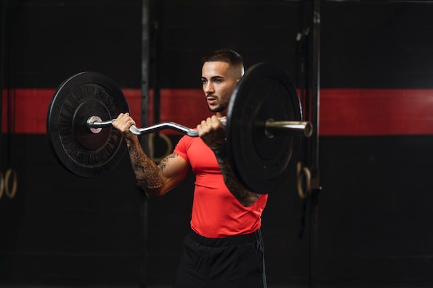 Tätowierter junger Mann, der in einem Fitnessstudio mit Gewichten und Rudergerät Sport treibt