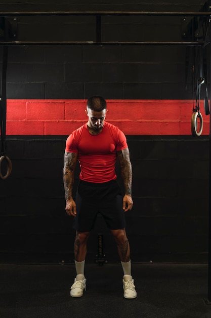 Tätowierter junger Mann, der in einem Fitnessstudio mit rotem T-Shirt Sport treibt