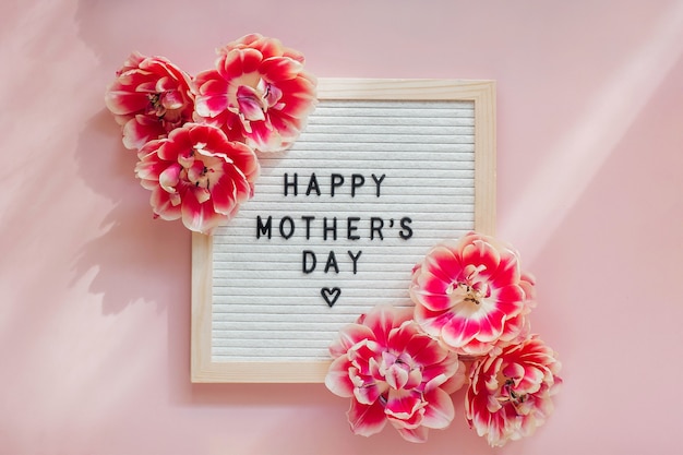Tafel mit einem Zeichen Glücklicher Muttertag auf einem rosa Tisch mit schönen Tulpenblumen.