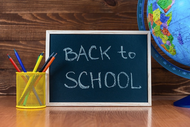 Tafel mit Text Back to School, Satz Buntstifte mit Glas und Globus auf hölzernem Hintergrund