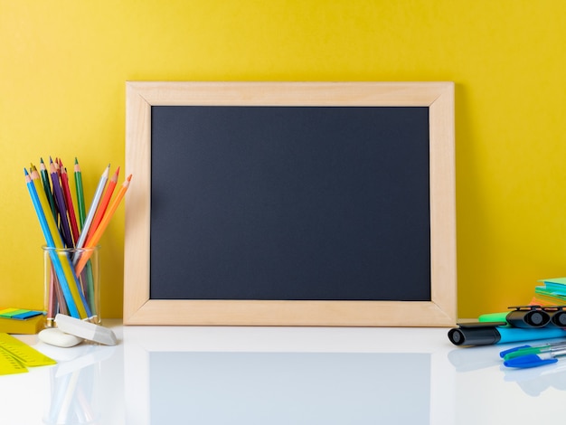 Tafel und Schulbedarf auf weißer Tabelle durch die gelbe Wand. Zurück zum Schulkonzept