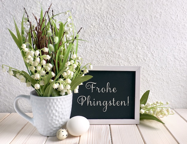 Tafel verziert mit Maiglöckchenblumen und Eiern, deutscher Text bedeutet "Happy Pentacost"