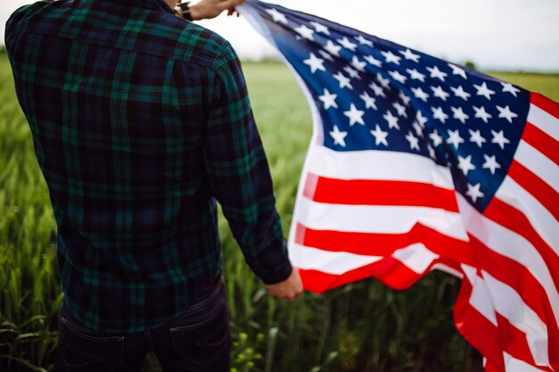 Tag der Unabhängigkeit. Ein Mann in einem karierten Hemd mit einer amerikanischen Flagge auf einem Feld.