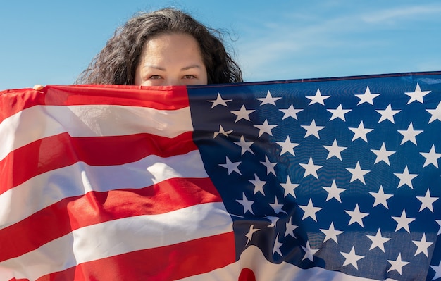 Tag der Unabhängigkeit. Patriotischer Feiertag. Eine Frau mit schwarzen Locken hält eine amerikanische Flagge. Das Konzept des Weltfriedens. USA feiern den 4. Juli.