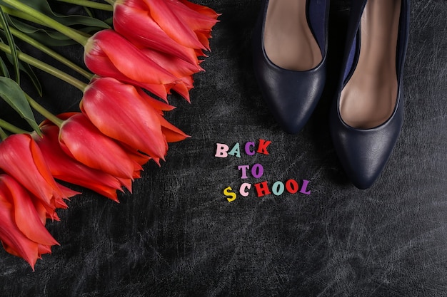 Tag des Wissens. Rote Tulpen mit Schuhen mit hohen Absätzen auf Kreidetafel. Zurück zur Schule. Ansicht von oben.