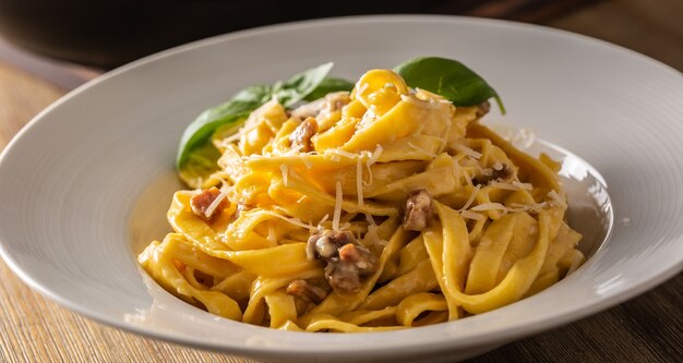 Tagliatelle carbonara de pasta de comida italiana con yema de huevo de pancetta parmesano y hojas de albahaca.