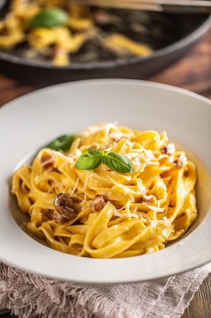 Tagliatelle carbonara de pasta de comida italiana con yema de huevo de pancetta parmesano y hojas de albahaca.