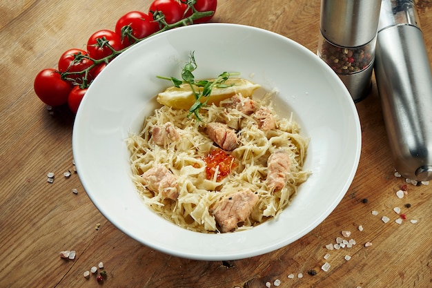 Foto tagliatelle caseiros italianos com salmão e parmesão em uma tigela bege em uma superfície de madeira. massa saborosa. copie o espaço