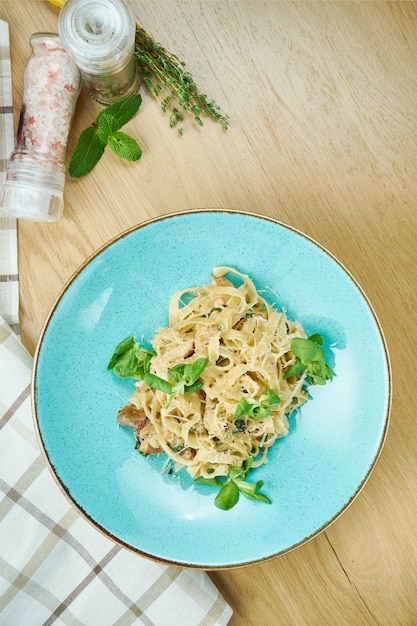 Tagliatelle com frango, molho branco e parmesão em uma tigela azul na mesa de madeira. massa italiana caseira tradicional. fechar-se