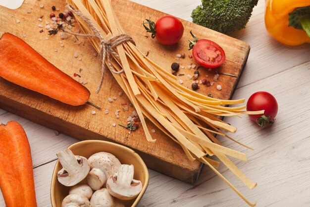 Tagliatelle de laranja artesanal cru com suco de cenoura, tomate, brócolis, cogumelos e especiarias na mesa de madeira branca. Cozinhando massa, copie o espaço