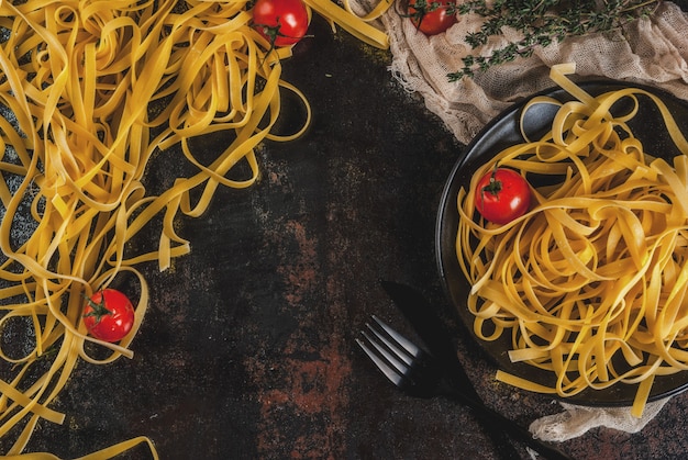 Tagliatelle de massa italiana tradicional, na mesa enferrujada de metal escuro com ingredientes para cozinhar o jantar - tomate, ervas, copyspace