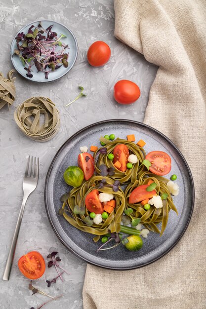 Tagliatelle grüne Spinatnudeln mit Tomaten-, Erbsen- und Mikrogrünsprossen auf einem grauen Betonhintergrund. Draufsicht, Nahaufnahme.