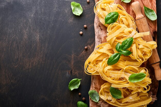 Tagliatelle. massa caseira, folhas de manjericão, farinha, pimenta, azeite, tomate cereja e rolo e faca de macarrão no fundo escuro de madeira velho. conceito de comida. brincar. horizontal com espaço de cópia.