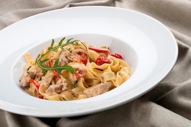 Tagliatelle mit Kaninchen und Paprika mit Sahnesauce in einem weißen Teller auf Textilhintergrund