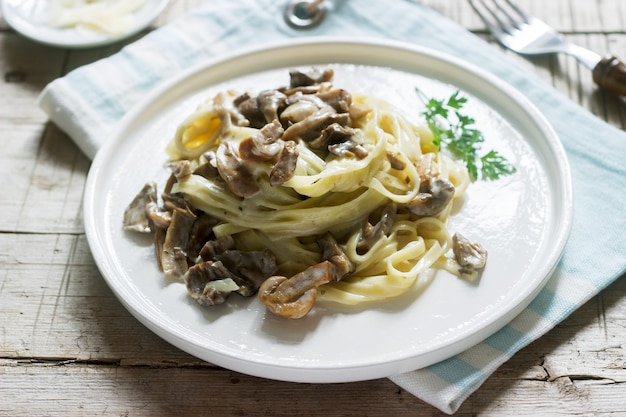 Tagliatelle mit Sahne und Waldpilzsauce in einem weißen Teller auf einem hölzernen Hintergrund. Rustikaler Stil.