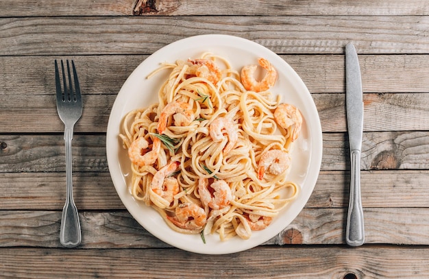 Tagliatelle de pasta con camarones en salsa cremosa en plato blanco sobre fondo rústico de madera Vista superior