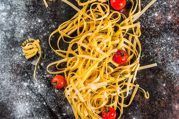 Tagliatelle de pasta italiana tradicional, sobre una mesa de metal oscuro oxidado con ingredientes para cocinar la cena - tomates, hierbas, vista superior del espacio de copia