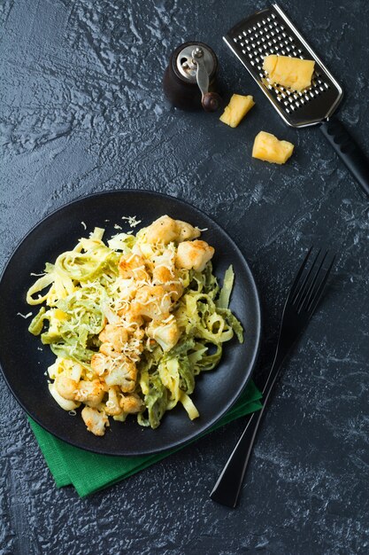 Tagliatelle de pasta en salsa cremosa con coliflor al horno en un plato sobre una superficie oscura