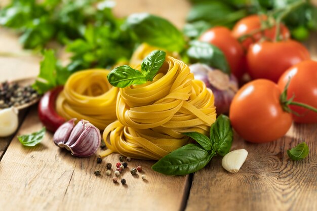 Tagliatelle sobre mesa de madera con hojas de albahaca, pimiento, ajo y perejil de cerca con espacio de copia, ingredientes de la comida italiana