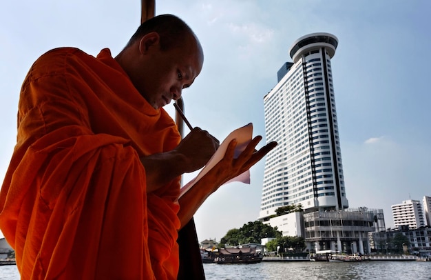 Tailandia, Bangkok, monje budista en un barco que cruza el río Chao Phraya (Templo de Arun en el fondo)