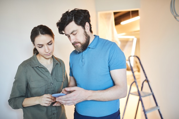 Foto taille hoch porträt des ehepaares mit smartphone für design-ideen beim renovieren des hauses zusammen, kopieren raum