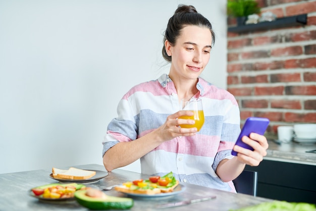 Taille hoch Porträt einer lächelnden jungen Frau, die das Frühstück zu Hause genießt und soziale Medien überprüft, Raum kopiert