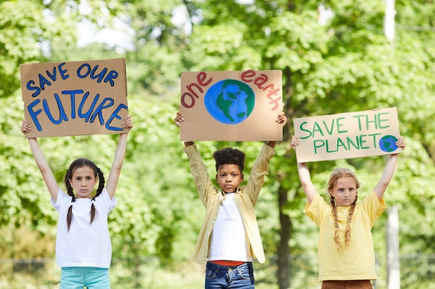Taille hoch Porträt von drei Kindern, die Schilder mit SAVE PLANET SAVE FUTURE halten, während sie für die Natur im Freien protestieren, Raum kopieren