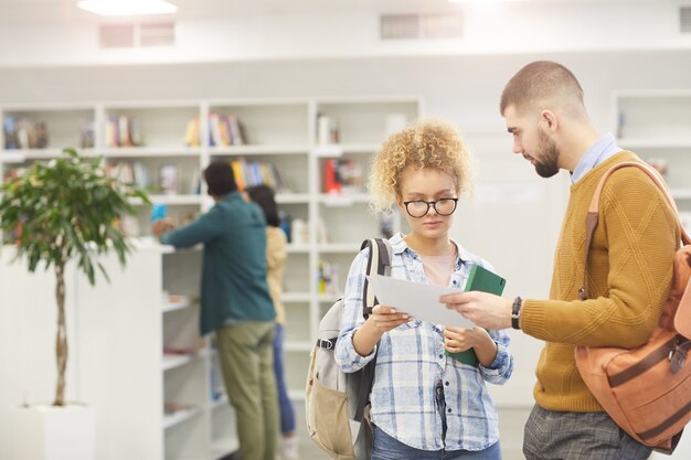 Taille hoch Porträt von einigen Studenten, die Papiere lesen, während sie in der Universitätsbibliothek stehen