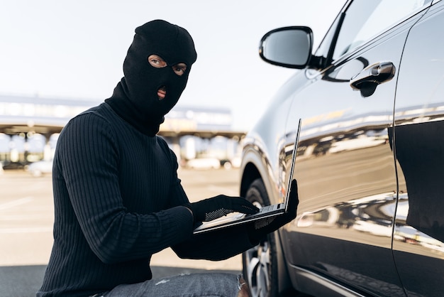 Taillenporträt des Autodiebs mit Laptop-Hacking-Alarmsystem, während Sie tagsüber in der Nähe des Autos sitzen. Stock Foto