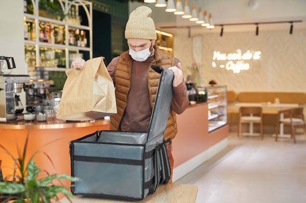 Taillenporträt des Lieferers mit Maske beim Verpacken von Bestellungen zum Einsacken im Café-Interieur, Kopierraum