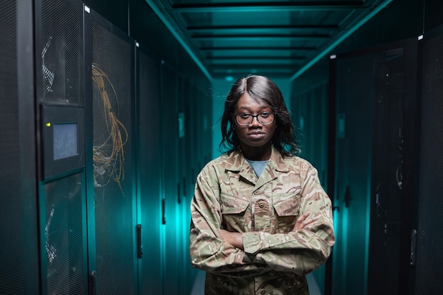 Taillenporträt einer harten afroamerikanischen Frau, die die Kamera anschaut, während sie im Serverraum mit futuristischem Hintergrund steht, Kopierraum