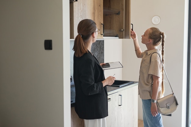 Taillenporträt einer Immobilienmaklerin, die der jungen Frau, die ein neues Haus kauft, eine Wohnungstour gibt