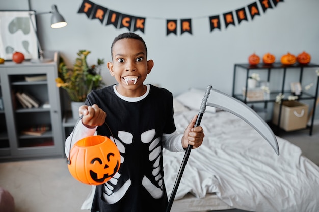 Taillenporträt eines afroamerikanischen Teenagers, der Halloween-Eimer hält, während er Grimassen bei...