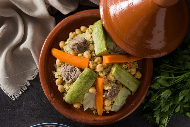 Tajine tradicional con verduras, garbanzos, carne y cuscús en pizarra negra. Vista superior