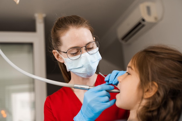 Taladro dental Dentista infantil perforando dientes de niña en clínica de odontología Relleno dental para paciente infantil