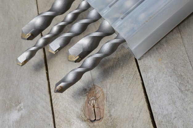 Los taladros con brocas de martillo con punta de carburo se encuentran en una caja de plástico sobre un fondo de madera. de cerca.