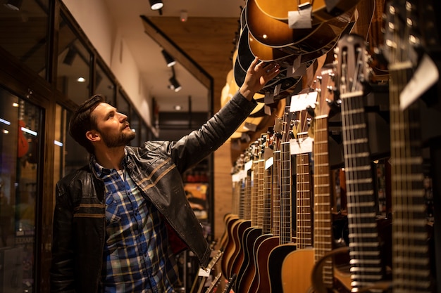 Talentierter Musiker in Lederjacke auf der Suche nach perfekter Gitarre im Musikladen.