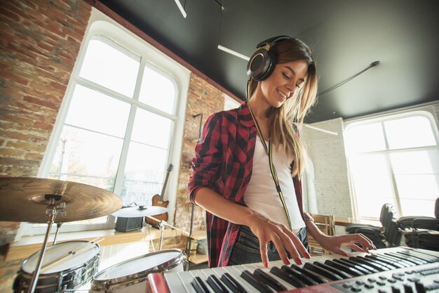 Talentierter Musiker, schöne Frau, die Musik aufnimmt, singt und Klavier spielt, während sie im Loft-Arbeitsplatz oder zu Hause steht. Konzept von Hobby, Musik, Kunst und Kreation. Erste Single erstellen.