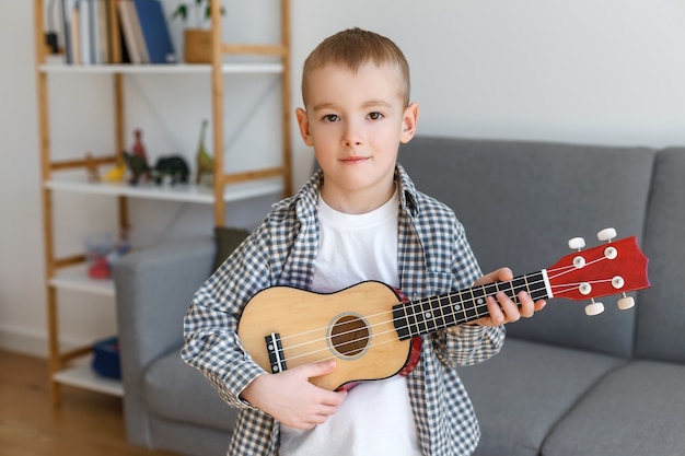 Talentiertes Kind, das zu Hause Sopran-Ukulele hält Vorschuljunge, der in der Freizeit Gitarre lernt