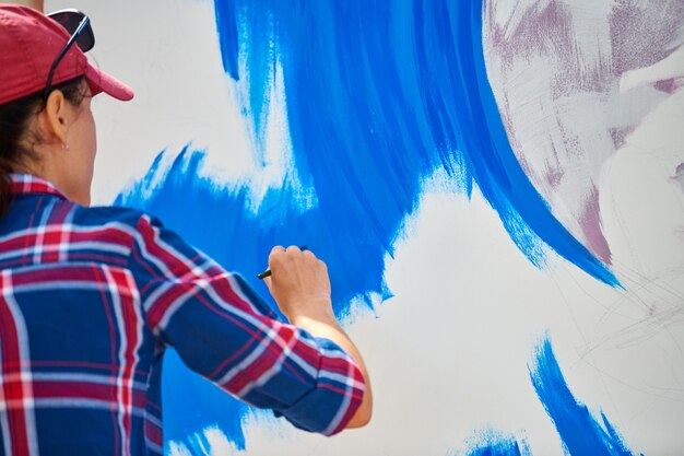 Talentoso artista femenino pintando sobre lienzo de madera trabajando en pintura al óleo abstracta moderna en el festival, gesticulando con trazos amplios con pincel. Concepto de bellas artes, creatividad y personas.