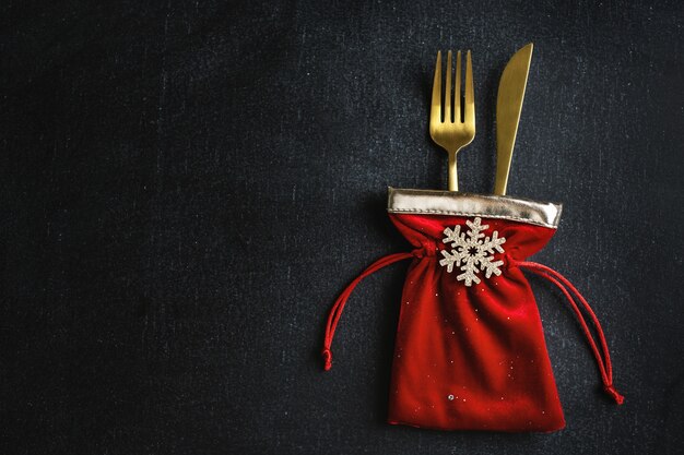 Talheres de Natal dourados em pequena bolsa têxtil com floco de neve e fita preta. Lay Flat.