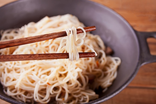 Tallarines asiáticos con la carne de vaca, verduras en wok con los palillos, fondo de madera rústico. Cena de estilo asiático. Fideos chinos japoneses