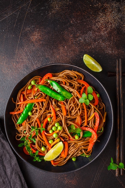 Tallarines del soba del alforfón del vegano con las verduras en la placa negra, visión superior.