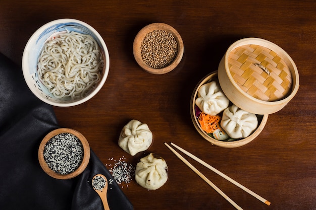 Foto tallarines de udon con semillas de sésamo; semillas de cilantro con albóndigas y palillos en mesa de madera