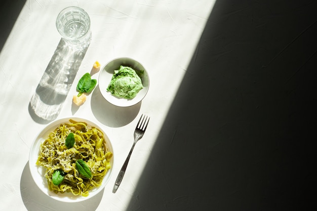 Tallarines verdes con espinacas y queso parmesano en un plato blanco sobre una mesa blanca luz dura y sombra ...