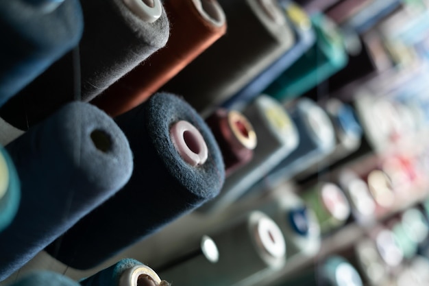 En un taller de costura, muchas bobinas de hilo de diferentes colores cuelgan de una pared de metal Concepto de sastrería y variedad de materiales