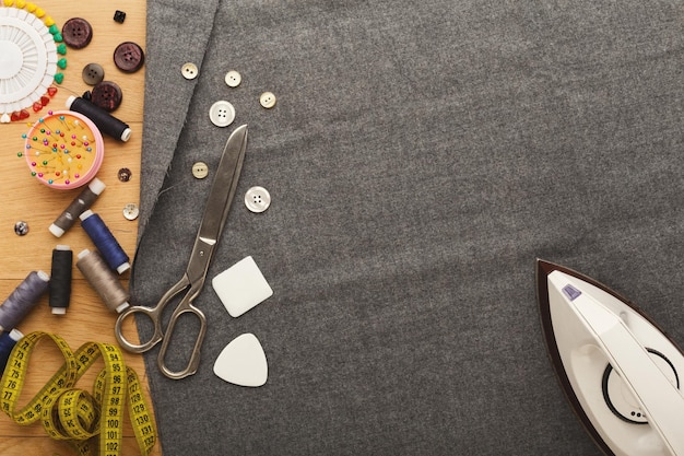 Taller de costura o diseñador de moda en el trabajo. Vista superior de la plaza de tela de planchado de manos femeninas. Mesa desordenada con accesorios de modista, espacio de copia